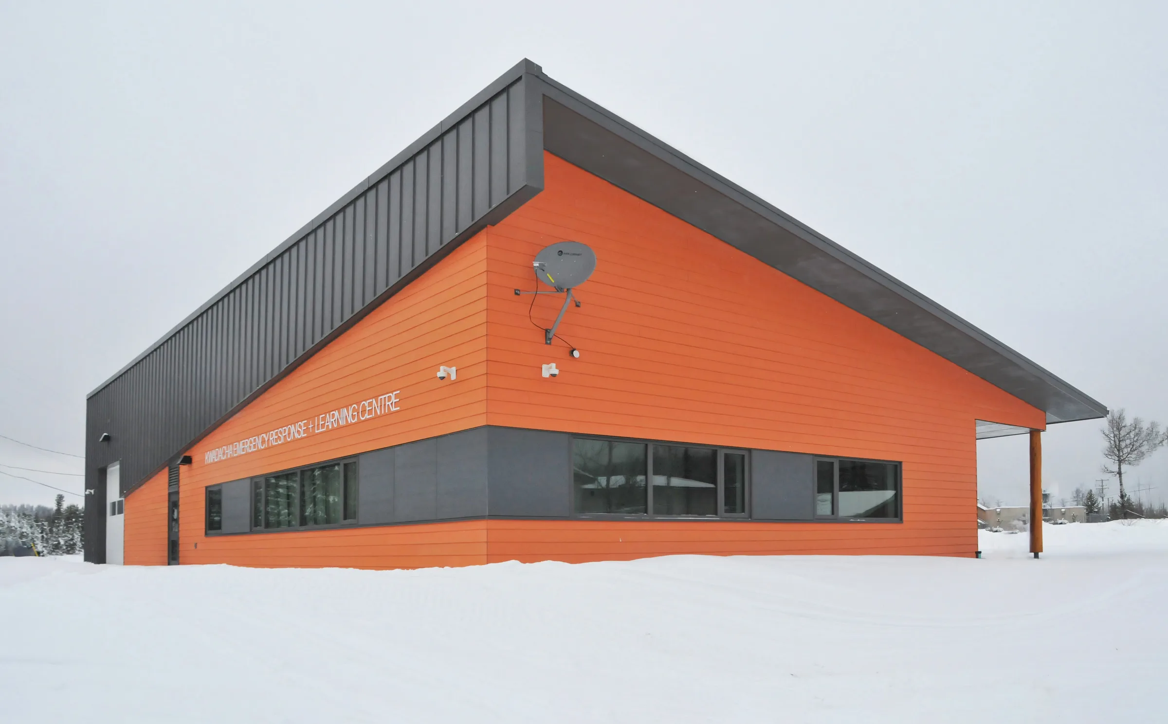 The completed centre in snow, its orange and dark metal cladding under a single sloping roof.