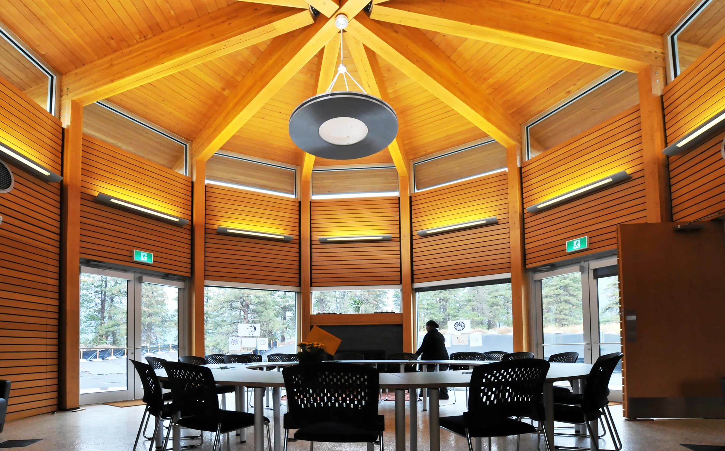 Sala comunitaria, techo radial de madera y ventanas altas que evocan vivienda semienterrada.