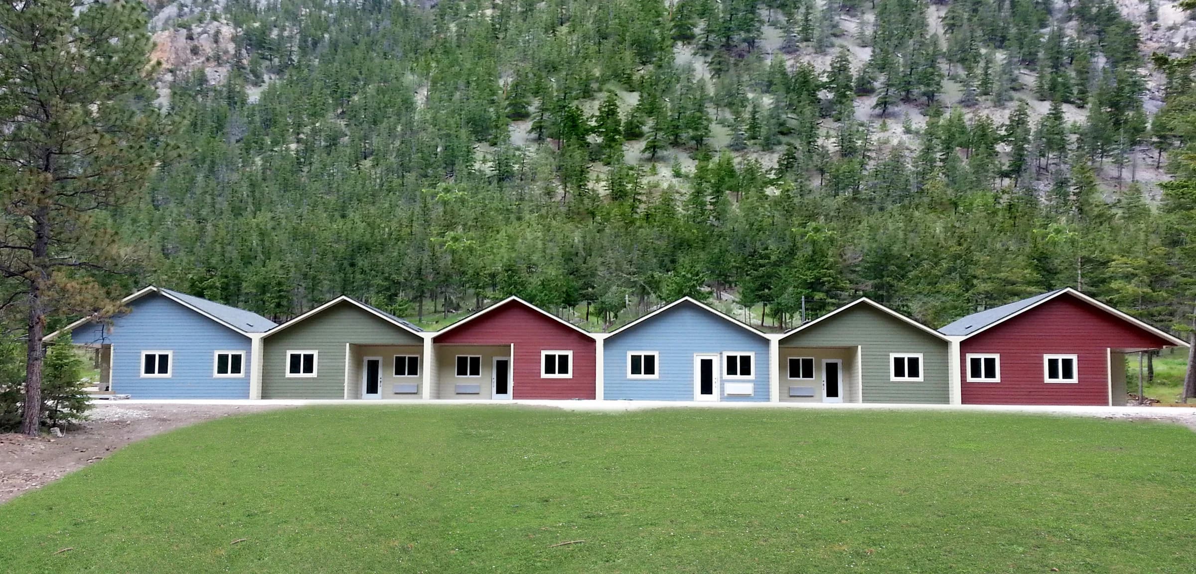 Viviendas terminadas azules, grises y rojas en ladera bajo bosque.